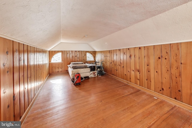 unfurnished bedroom featuring vaulted ceiling, wood finished floors, wood walls, and a textured ceiling