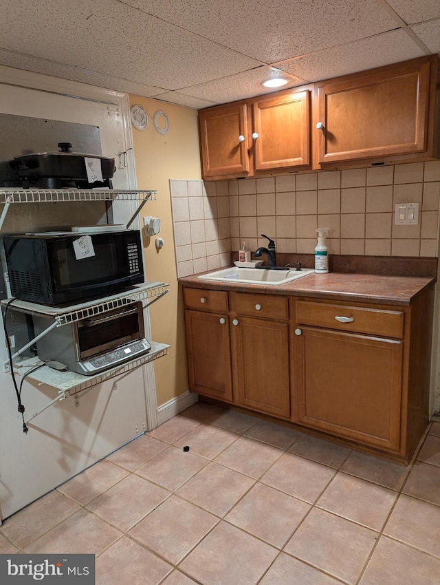 kitchen featuring tasteful backsplash, black microwave, light tile patterned flooring, brown cabinets, and a sink