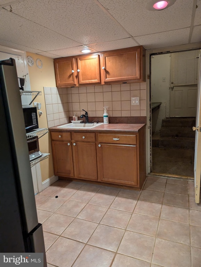 kitchen featuring light tile patterned floors, a sink, a paneled ceiling, brown cabinetry, and black microwave