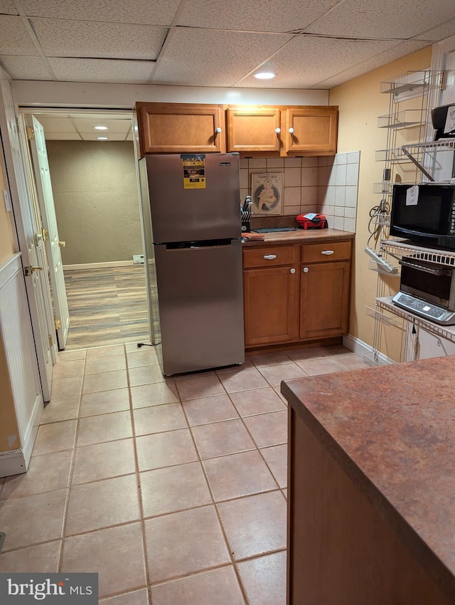 kitchen with brown cabinetry, freestanding refrigerator, and light tile patterned floors