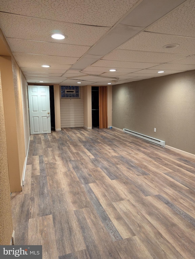 finished basement featuring baseboards, recessed lighting, a baseboard radiator, a drop ceiling, and wood finished floors