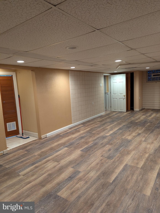 finished below grade area featuring a paneled ceiling, baseboards, recessed lighting, visible vents, and wood finished floors