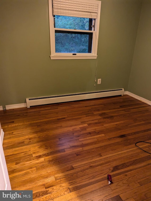 empty room featuring a baseboard radiator, baseboards, and wood finished floors