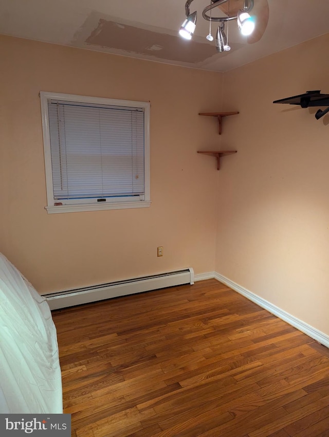 unfurnished bedroom featuring a chandelier, a baseboard heating unit, baseboards, and wood finished floors