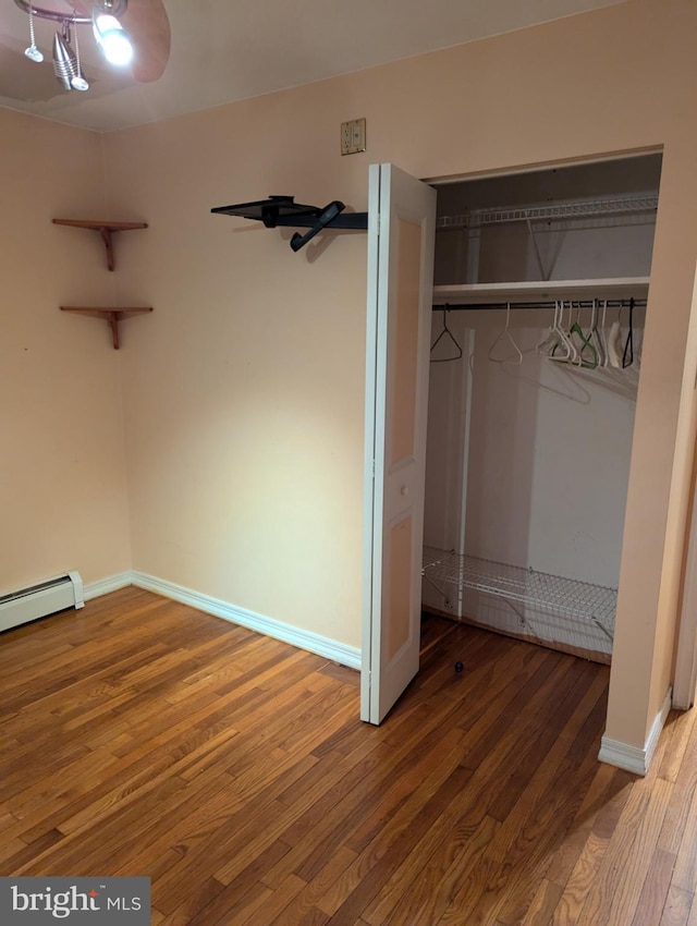 unfurnished bedroom featuring a baseboard radiator, wood finished floors, baseboards, and a closet