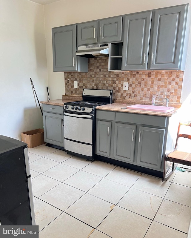 kitchen with light tile patterned floors, gray cabinetry, backsplash, range, and ventilation hood