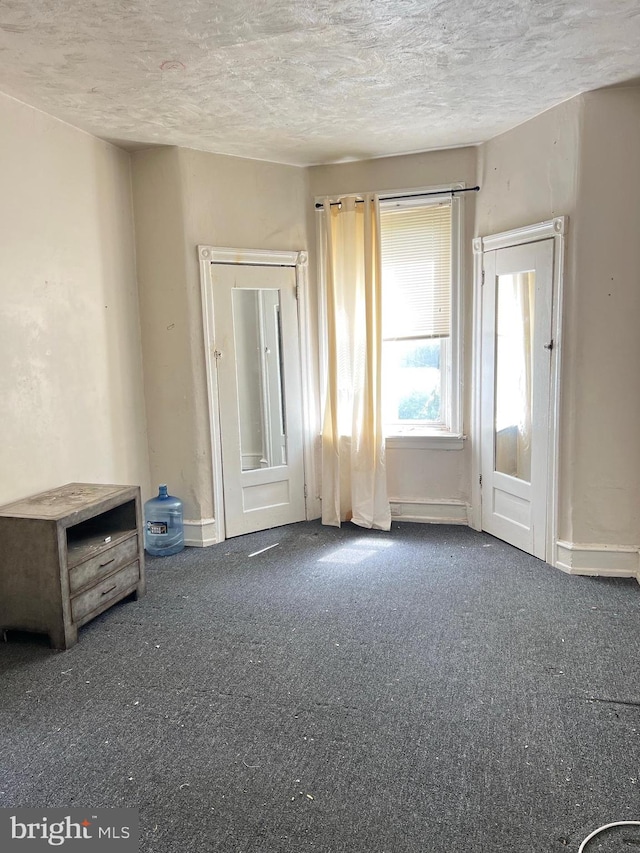 spare room featuring a textured ceiling and dark colored carpet