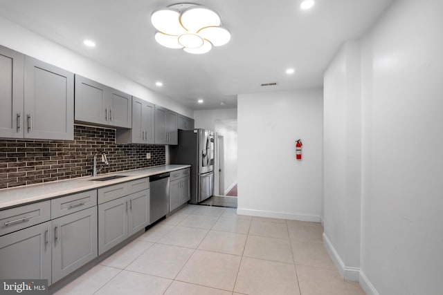 kitchen with light tile patterned flooring, sink, gray cabinetry, backsplash, and stainless steel appliances