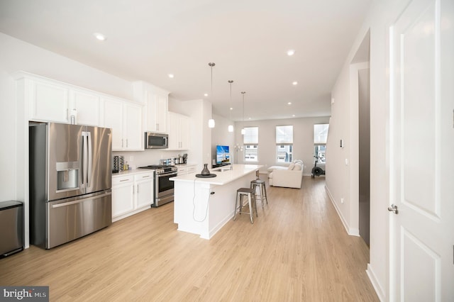 kitchen featuring white cabinets, a kitchen breakfast bar, stainless steel appliances, a center island with sink, and decorative light fixtures