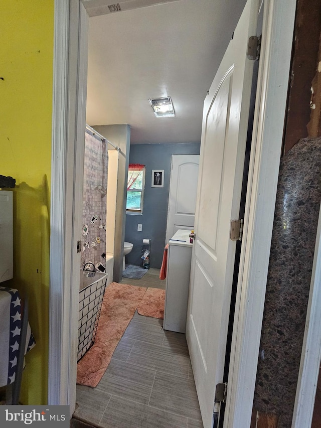 bathroom featuring toilet, walk in shower, and stacked washer and dryer