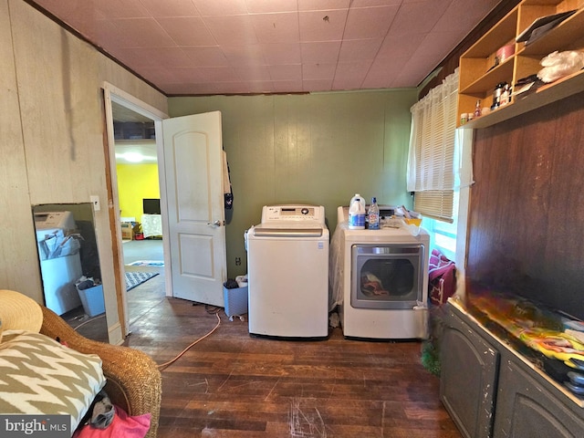 clothes washing area featuring wooden walls, washing machine and dryer, and dark hardwood / wood-style flooring