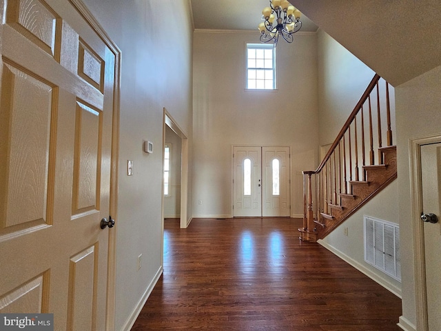 foyer with ornamental molding, an inviting chandelier, and dark wood-type flooring