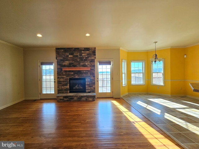 unfurnished living room featuring a stone fireplace, crown molding, hardwood / wood-style floors, and an inviting chandelier