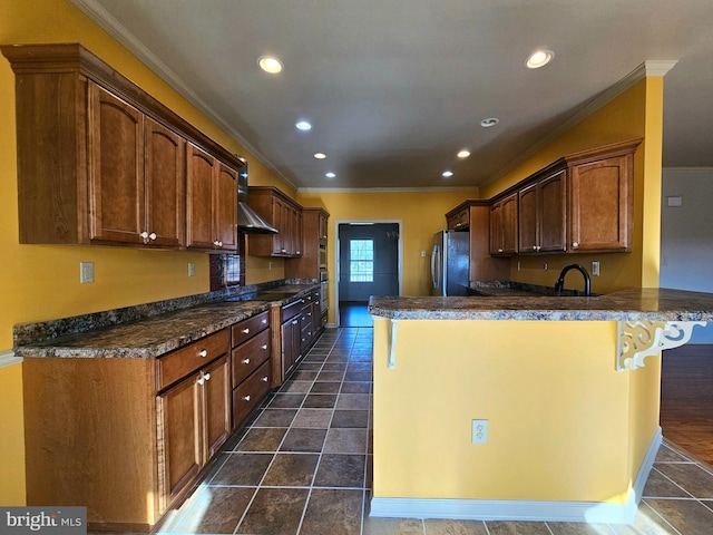 kitchen with kitchen peninsula, stainless steel fridge, ornamental molding, dark tile patterned floors, and sink