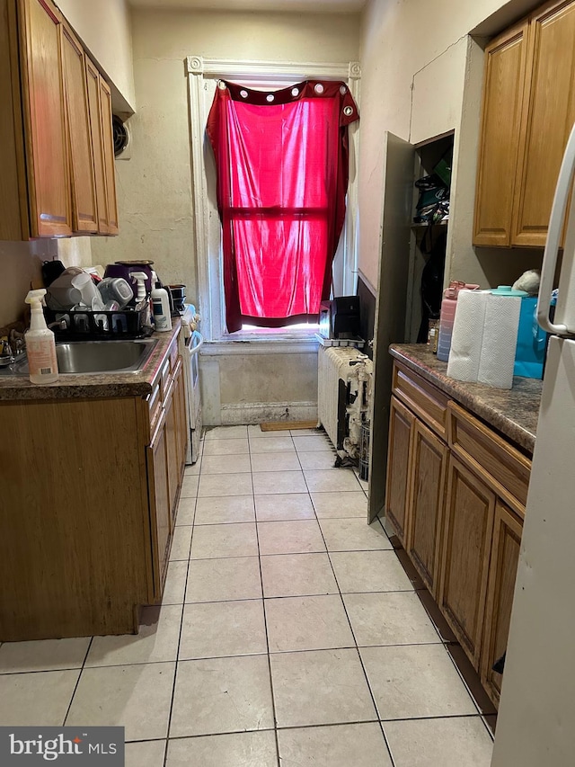 kitchen featuring white range oven, light tile patterned flooring, sink, and radiator heating unit