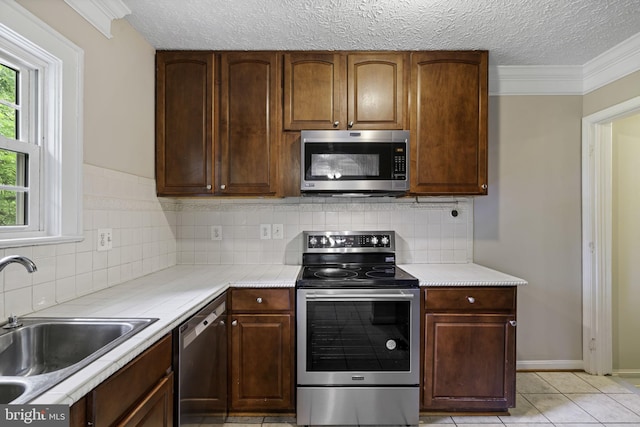 kitchen with appliances with stainless steel finishes, light countertops, a textured ceiling, a sink, and light tile patterned flooring