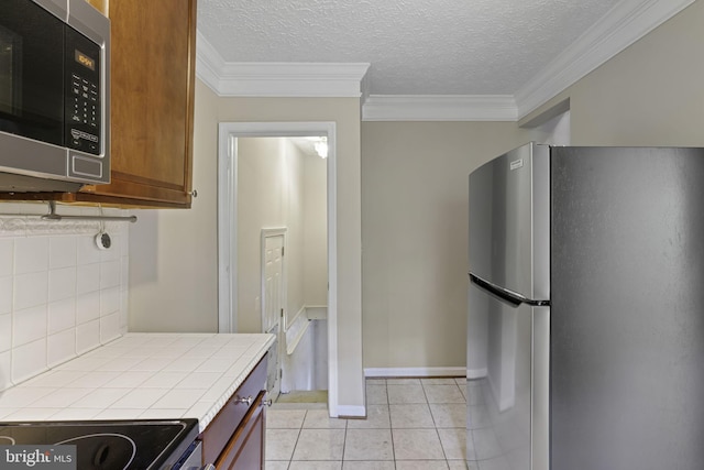 kitchen featuring light tile patterned flooring, appliances with stainless steel finishes, brown cabinets, tasteful backsplash, and crown molding