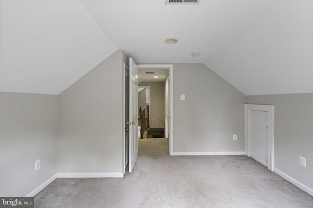 additional living space with baseboards, vaulted ceiling, visible vents, and light colored carpet