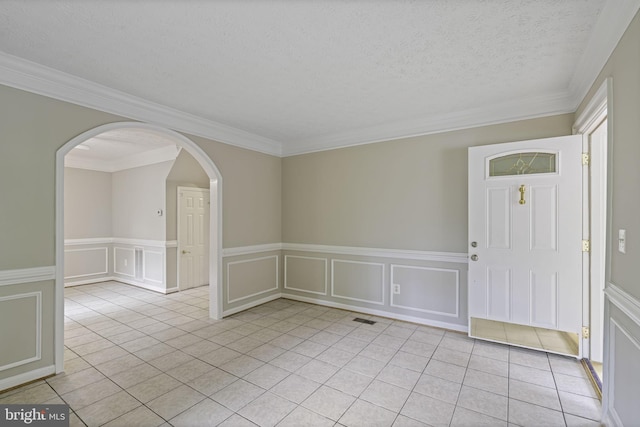 spare room featuring arched walkways, visible vents, a decorative wall, light tile patterned flooring, and a textured ceiling