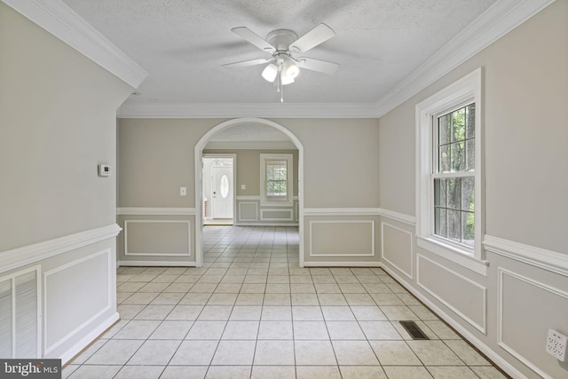 empty room featuring arched walkways, light tile patterned floors, visible vents, a decorative wall, and a textured ceiling