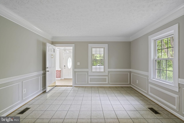 empty room featuring light tile patterned floors, a textured ceiling, a decorative wall, visible vents, and ornamental molding