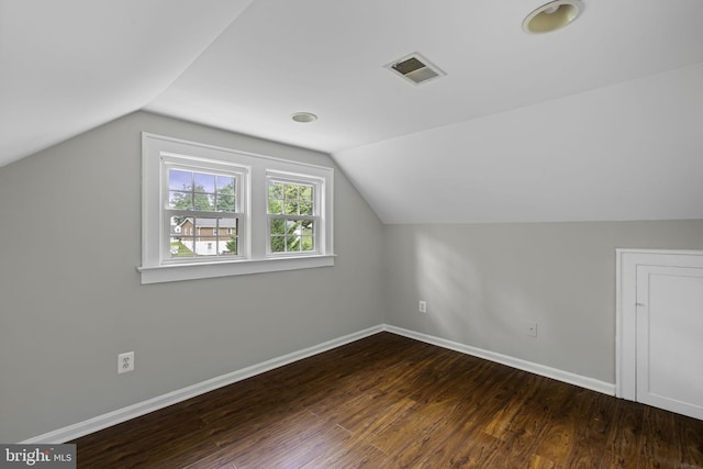 additional living space with lofted ceiling, dark wood-type flooring, visible vents, and baseboards