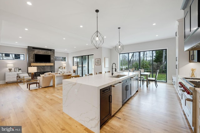 kitchen with light hardwood / wood-style floors, a large island with sink, a fireplace, pendant lighting, and sink