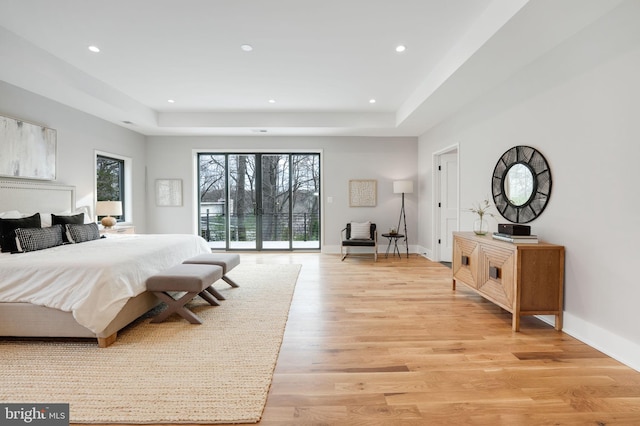 bedroom with light wood-type flooring, a tray ceiling, and access to exterior