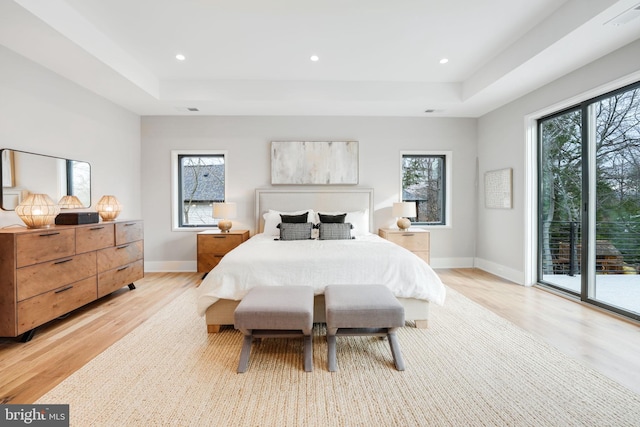 bedroom with light hardwood / wood-style flooring, access to exterior, and a tray ceiling