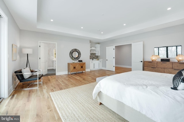 bedroom with light wood-type flooring, ensuite bath, and a raised ceiling