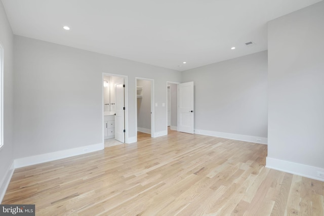 unfurnished bedroom featuring a spacious closet, light wood-type flooring, a closet, and ensuite bathroom