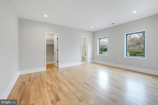 unfurnished bedroom with light wood-type flooring, ensuite bathroom, a walk in closet, and a closet