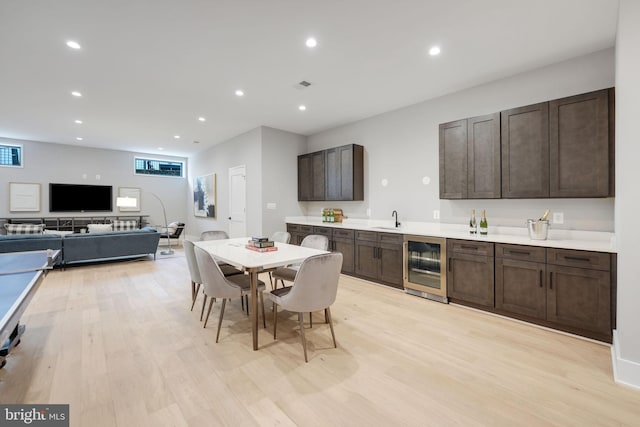 kitchen with dark brown cabinets, beverage cooler, light hardwood / wood-style floors, and sink