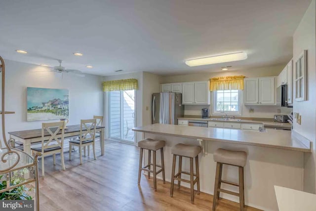 kitchen with white cabinets, a kitchen bar, light hardwood / wood-style flooring, appliances with stainless steel finishes, and ceiling fan