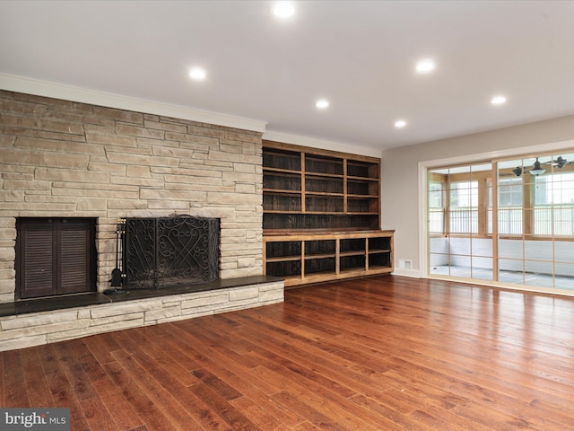 unfurnished living room with wood-type flooring, a stone fireplace, and crown molding