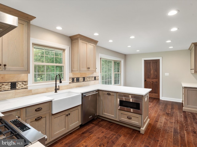 kitchen with appliances with stainless steel finishes, kitchen peninsula, decorative backsplash, and dark wood-type flooring