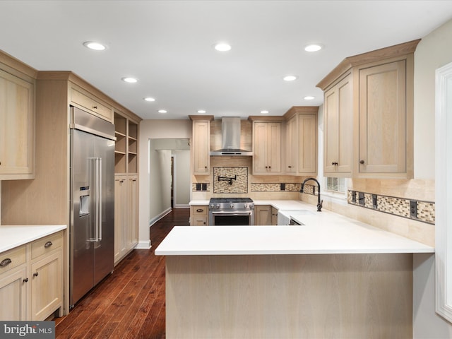 kitchen with sink, kitchen peninsula, premium appliances, wall chimney exhaust hood, and dark hardwood / wood-style floors