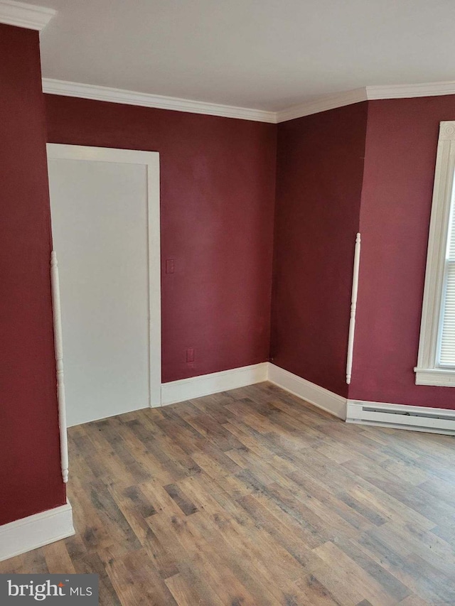 unfurnished room with wood-type flooring, ornamental molding, and a baseboard heating unit