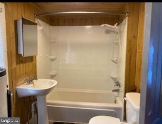 bathroom with  shower combination, wood walls, and toilet