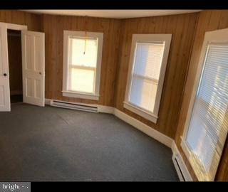 unfurnished room with a baseboard radiator, wooden walls, and dark carpet