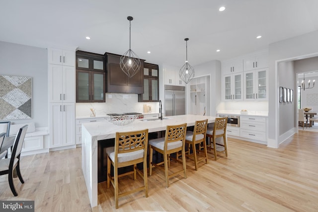 kitchen with sink, a kitchen island with sink, appliances with stainless steel finishes, a kitchen breakfast bar, and light hardwood / wood-style floors