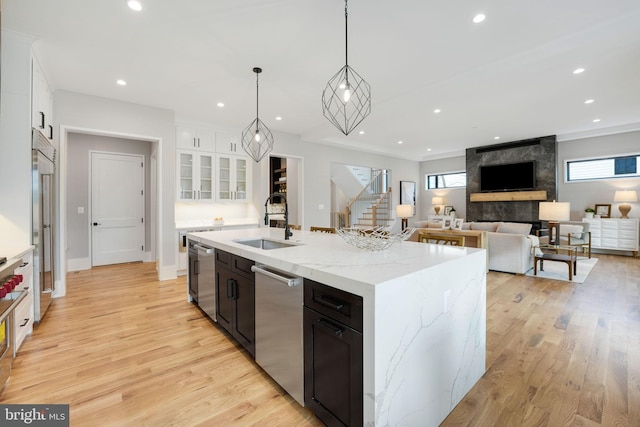 kitchen with pendant lighting, an island with sink, white cabinets, a fireplace, and light hardwood / wood-style flooring