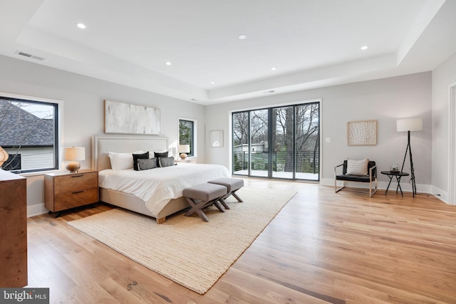 bedroom with access to outside, a tray ceiling, and light hardwood / wood-style floors