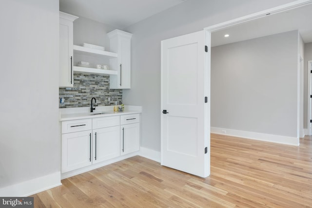 bar featuring tasteful backsplash, sink, light hardwood / wood-style flooring, and white cabinets