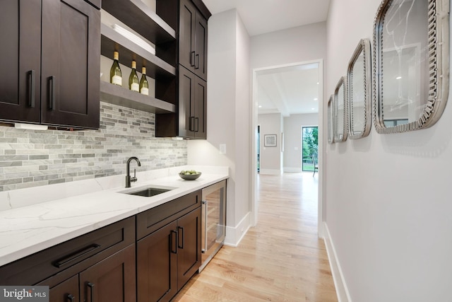 kitchen with light stone counters, backsplash, dark brown cabinets, light hardwood / wood-style flooring, and sink