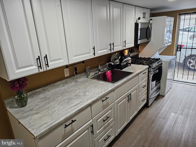 kitchen with white cabinets, sink, appliances with stainless steel finishes, washer / dryer, and light wood-type flooring