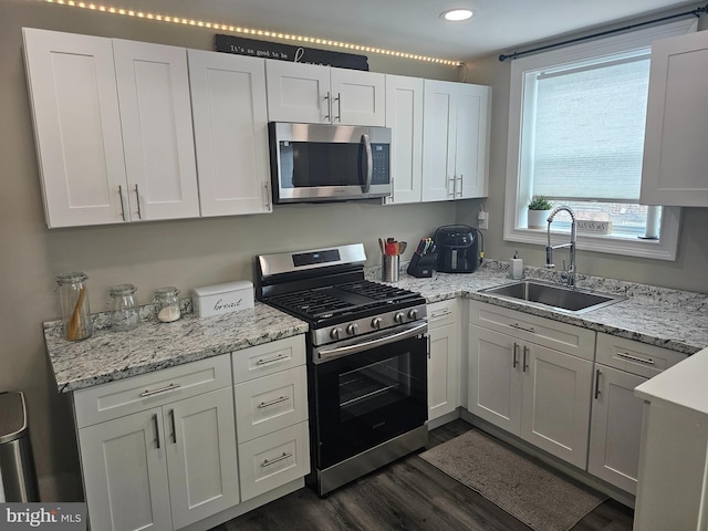 kitchen with light stone counters, sink, white cabinets, stainless steel appliances, and dark hardwood / wood-style flooring