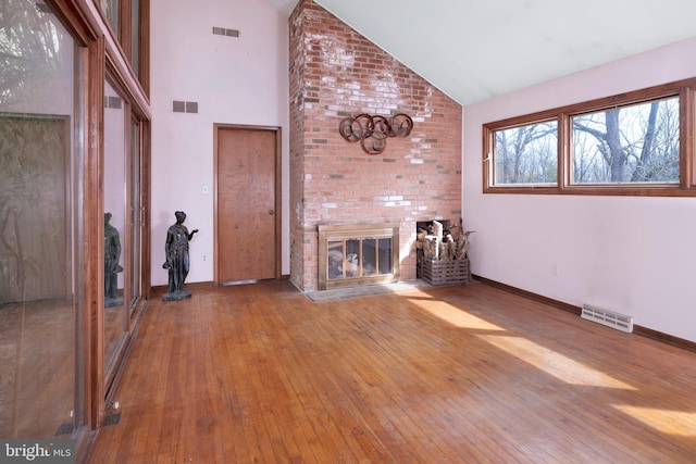 unfurnished living room with hardwood / wood-style floors, high vaulted ceiling, and a brick fireplace