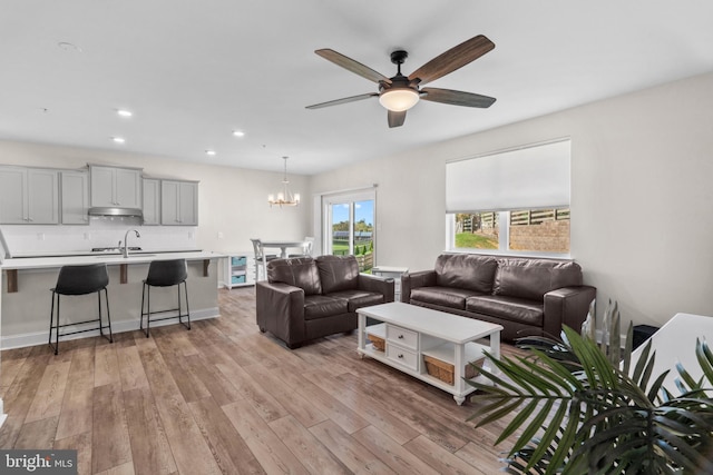 living room with ceiling fan with notable chandelier, sink, and light wood-type flooring