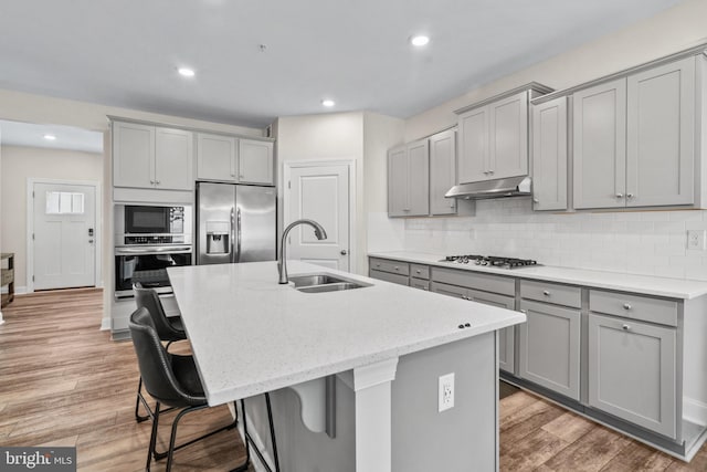 kitchen with an island with sink, sink, wood-type flooring, stainless steel appliances, and a kitchen bar